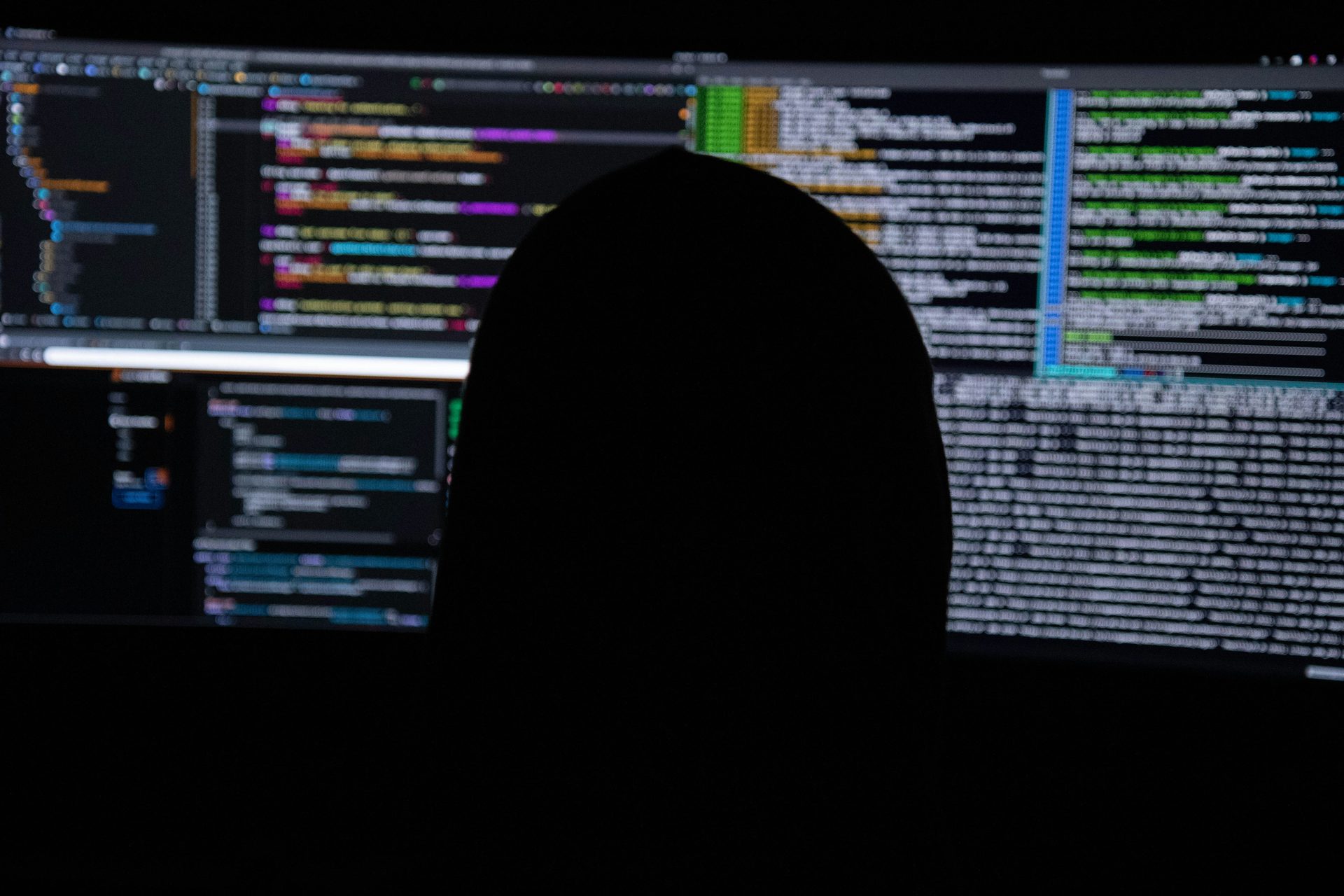 A silhouetted figure at screens of code, the view an attacker has